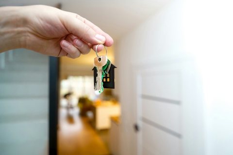 Une main tend un trousseau de clés dans l'entrée d'un appartement lumineux